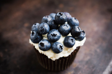 Homemade muffin with blueberry and cream cheese frosting on the rustic background. Selective focus.