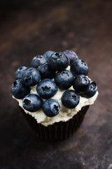Homemade muffin with blueberry and cream cheese frosting on the rustic background. Selective focus.