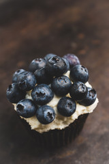 Homemade muffin with blueberry and cream cheese frosting on the rustic background. Selective focus.