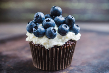 Homemade muffin with blueberry and cream cheese frosting on the rustic background. Selective focus.