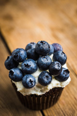 Homemade muffin with blueberry and cream cheese frosting on the rustic background. Selective focus.