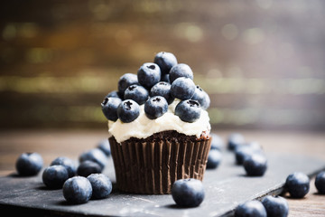Homemade muffin with blueberry and cream cheese frosting on the rustic background. Selective focus.