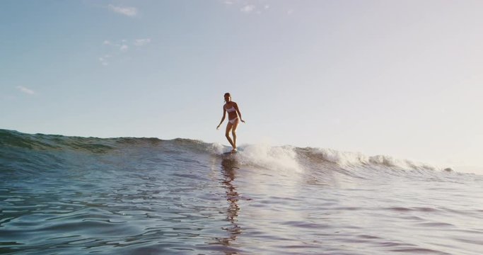 Young smiling woman surfing a wave in slow motion, walking to the nose of her longboard to hang five on summer wave at sunset, surfing lifestyle stoke