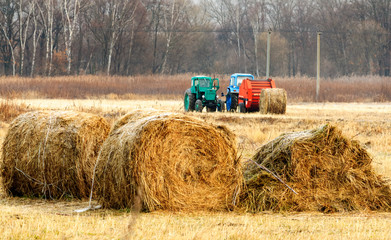 Tractors for harvesting dry grass in bales of straw in the field in the autumn. Special agricultural machinery. In the foreground are bales of straw. Shallow depth of field.