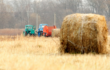 Tractors for harvesting dry grass in bales of straw in the field in the autumn. Special agricultural machinery. In the foreground are bales of straw. Shallow depth of field.