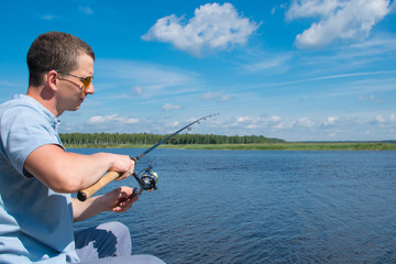 a man in yellow glasses,close-up, against a beautiful landscape, holding a spinning to pull the catch out of the water