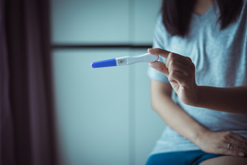 Close up female hands holding pregnancy test after testing  in her bedroom