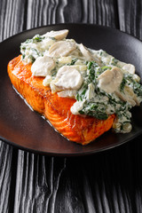 whole salmon fillet is baked to perfection, then it's finished with a topping of spinach, mushrooms, garlic and cream close up on the plate. vertical