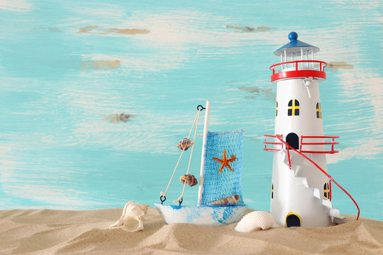 vacation and summer concept with vintage boat, starfish, lighthouse and seashells over beach sand infront of pastel blue background