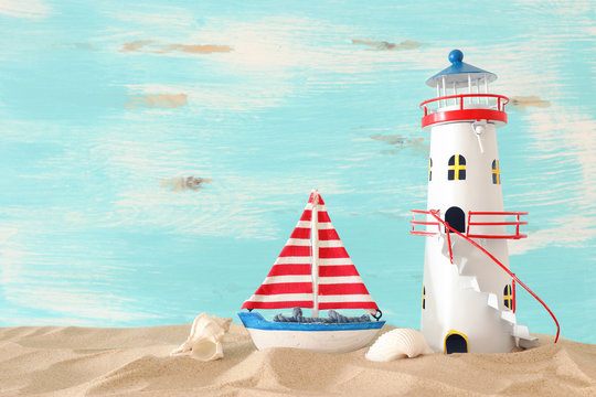 vacation and summer concept with vintage boat, starfish, lighthouse and seashells over beach sand infront of pastel blue background