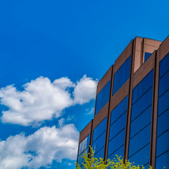 Fototapeta premium Frame Square Modern building with blue glass wall against blue sky with fluffy clouds