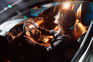 Fashionable young woman in a car in the night and colour light behing her