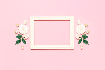 Flowers composition. Wooden white photo frame, white fresh roses and green leaves on gentle pink background. Flat lay, top view, copy space. Flower card, greeting, holiday mockup. Valentine's Day