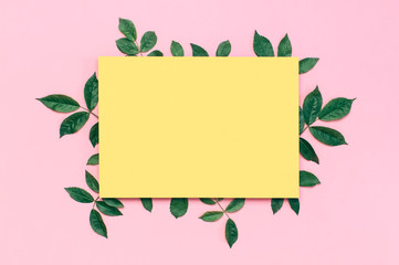 Flowers composition. Yellow blank paper, fresh green rose leaves on gentle pink background. Flat lay, top view, copy space. Flower card, greeting, holiday mockup. Valentine's Day background