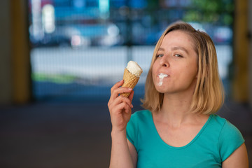 Portrait of a cute girl in a green dress is walking outside and eating dessert. Beautiful blonde enjoying a cone with ice cream on a beautiful summer day. Life is a pleasure