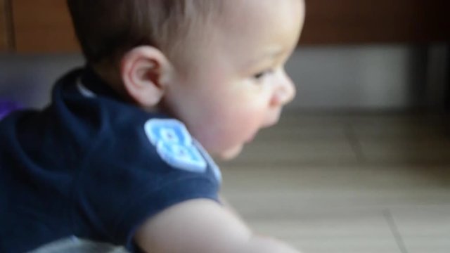 cute seven months old baby boy trying to reach dummy on the floor
