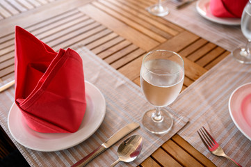 Dining wooden table set with ceramic tableware, silver utensil, red napkin and water