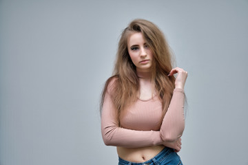 Naklejka premium A photo portrait of a beautiful woman girl on a light gray background with long beautiful hair in a pink sweater and blue jeans is standing right in front of the camera and smiling.