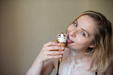 Sexy blonde licks a waffle cone. Ice cream is melting, erotically draining through the body of an attractive woman. Beautiful girl smeared with ice cream.