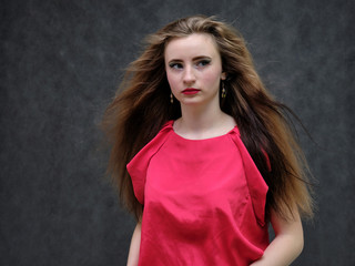 Fototapeta premium Photo portrait of a beautiful girl of the woman on a dark gray background with long beautiful hair in a red sleeveless jacket standing right in front of the camera and smiling.