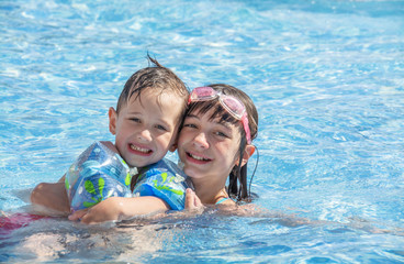 Fototapeta na wymiar Older sister and younger brother swim in the outdoor children's pool