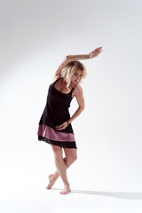 Photo of long-haired blonde in black dress looking down dancing in studio