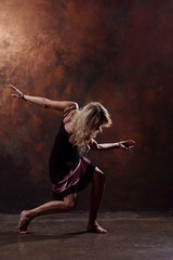 Fototapeta na wymiar Full-length photo of young blonde dancer in short black dress on brown background