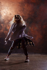Fototapeta na wymiar Photo of young blonde dancer in torn jeans and sneakers on dark brown background