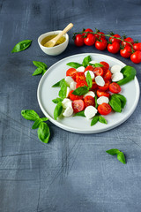 Italian Caprese salad: red tomatoes, fresh organic mozzarella and Basil, Italian cuisine. Healthy lunch. Top view on gray stone table