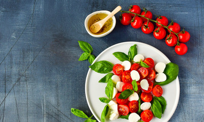 Italian Caprese salad: red tomatoes, fresh organic mozzarella and Basil, Italian cuisine. Healthy lunch. Top view on gray stone table