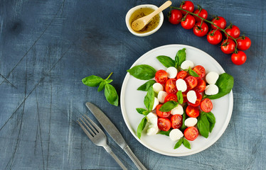 Italian Caprese salad: red tomatoes, fresh organic mozzarella and Basil, Italian cuisine. Healthy lunch. Top view on gray stone table