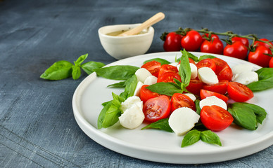 Italian Caprese salad: red tomatoes, fresh organic mozzarella and Basil, Italian cuisine. Healthy lunch. Top view on gray stone table