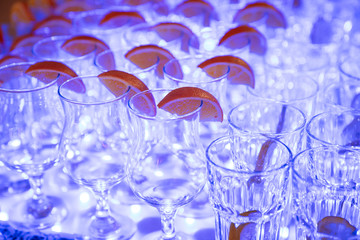 Glasses for alcoholic beverages with lemon on table, blue light