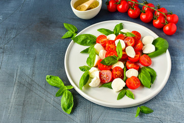 Italian Caprese salad: red tomatoes, fresh organic mozzarella and Basil, Italian cuisine. Healthy lunch. Top view on gray stone table