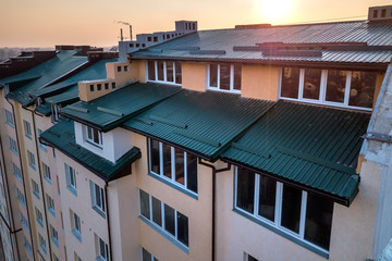 Fototapeta na wymiar Aerial view of attic annex room exterior with plastic windows, roof and walls covered with green metal siding planks, new gutter system on top of high multi-storey apartment building.