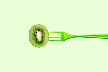 Kiwi on green plastic fork against pastel green background. Juicy summer colors concept. Minimal style.