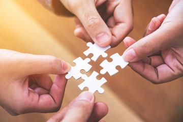 Closeup image of many people hands holding and putting a piece of white jigsaw puzzle together