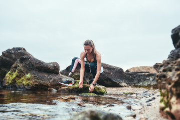 Woman in sportswear with prosthetic leg taking water in her hand from the river