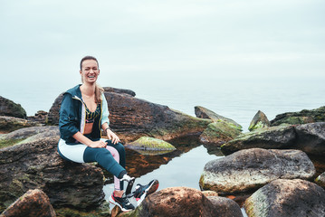 I am happy Cheerful disabled athlete woman in sportswear with prosthetic leg sitting on the stone and looking at camera with smile.