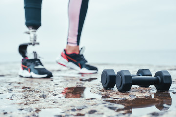 Strong and healthy. Cropped image of woman with prosthetic leg and dumbbells lying in front of the...