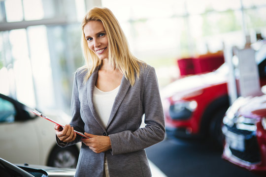 Portrait of beautiful saleswoman standing inside vehicle showroom