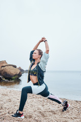 Yoga training. Vertical photo of strong disabled athlete woman with prosthetic leg standing in yoga pose at the beach.