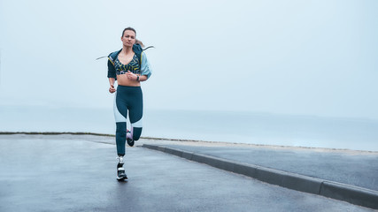 You are stronger than you think. Amazing strong disabled woman in sportswear is running outdoors near the sea - Powered by Adobe