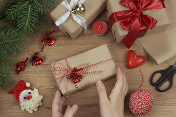 Fototapeta na wymiar Female hands holding Christmas gift box on wooden background with Fir branches, candles. Xmas and Happy New Year theme, bokeh, sparkling, glowing. Flat lay, top view