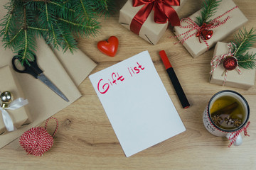 Gift list for New Year. Holiday decorations and notebook with gift list on wooden rustic table, flat lay style. Planning concept.