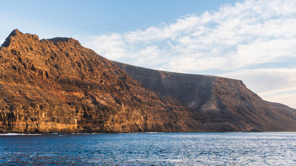 The amazing volcanic rugged sheer cliffs of Lanzarote Island, Canary, Spain as seen from a ferry crossing between Orzola and La Graciosa Island.