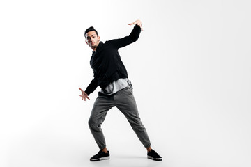 Stylish young dancer wearing a black sweatshirt and gray pants is dancing hip-poh on a white...