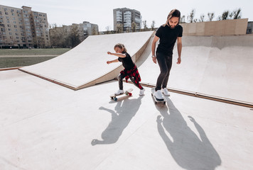 Father and his little son dressed in the casual clothes ride skateboards in a skate park with slides at the sunny day