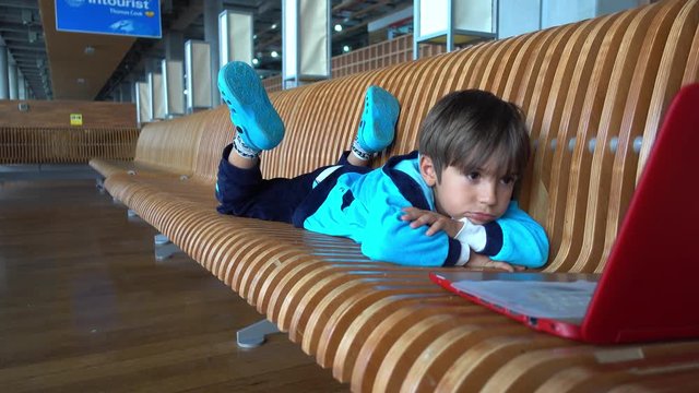 Dalaman Airport, Turkey - 24th of May 2018: 4K Tired bored kid in front of laptop in the airport looks into camera, crystal child