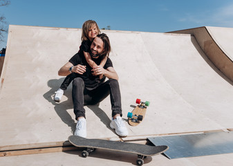 Happy young father and his son dressed in the stylish casual clothes are sitting in an embrace together on the slide next to the skateboards in a skate park at the sunny warm day © Leika production